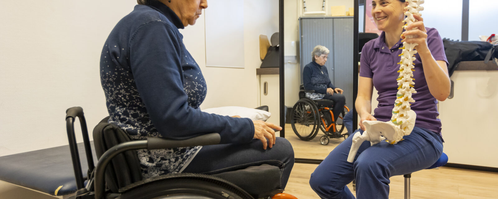 Behandelaar geeft uitleg over de houding aan een dwarslaesiepatiënt in een rolstoel